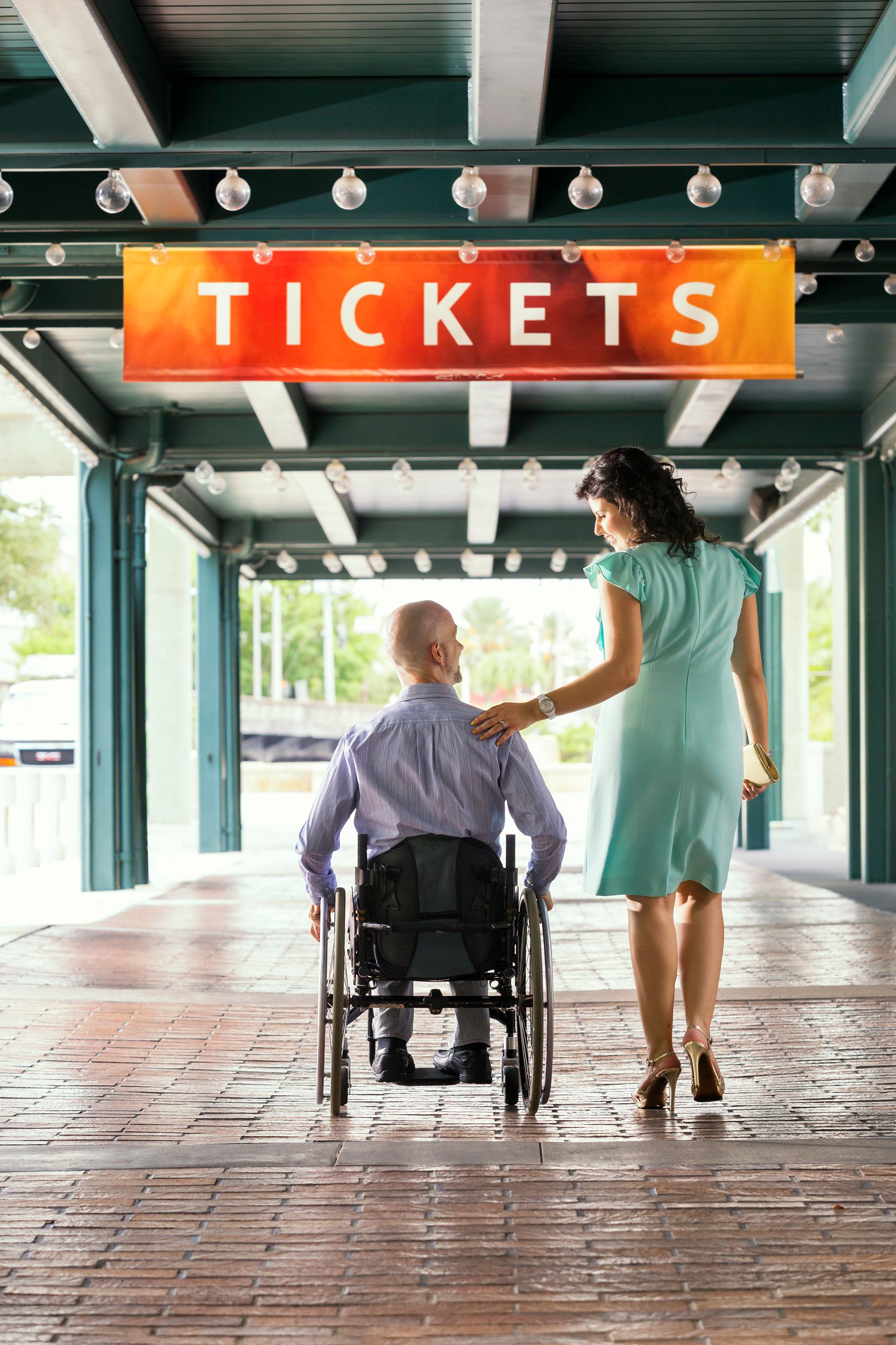 Man in wheelchair at Straz box office with woman in teal dress.