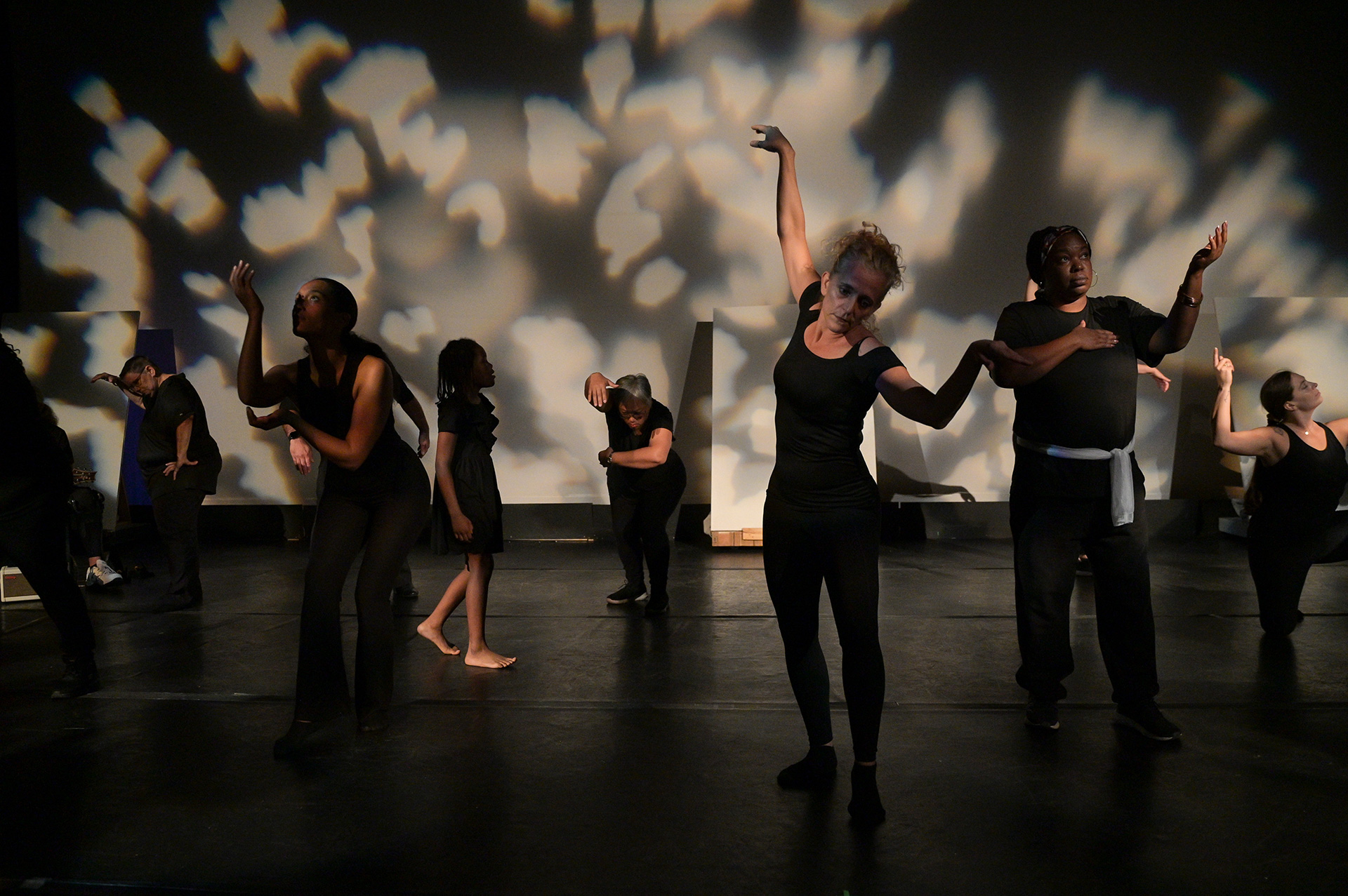Performers in a studio space posing in different poses with their shadows being cast against the wall.