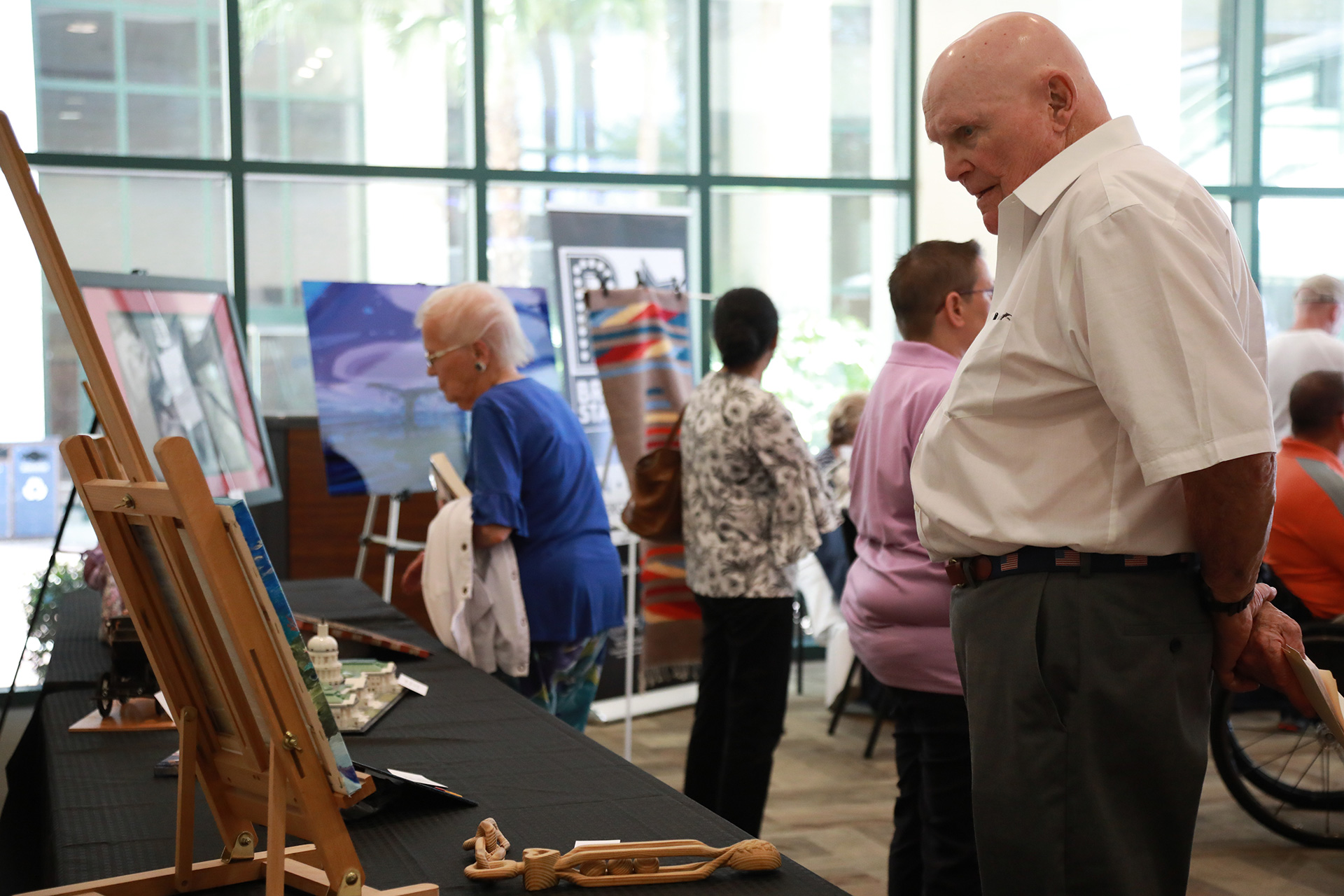 People looking at artwork set out on tables in an indoor space.