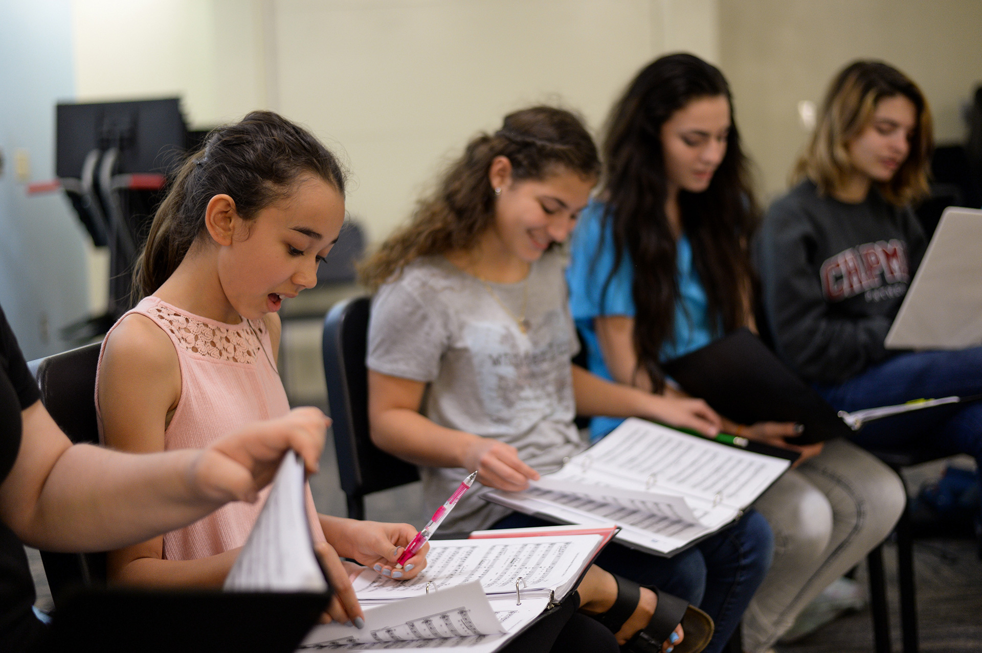 Patel students sitting in a row of chairs looking at sheet music.