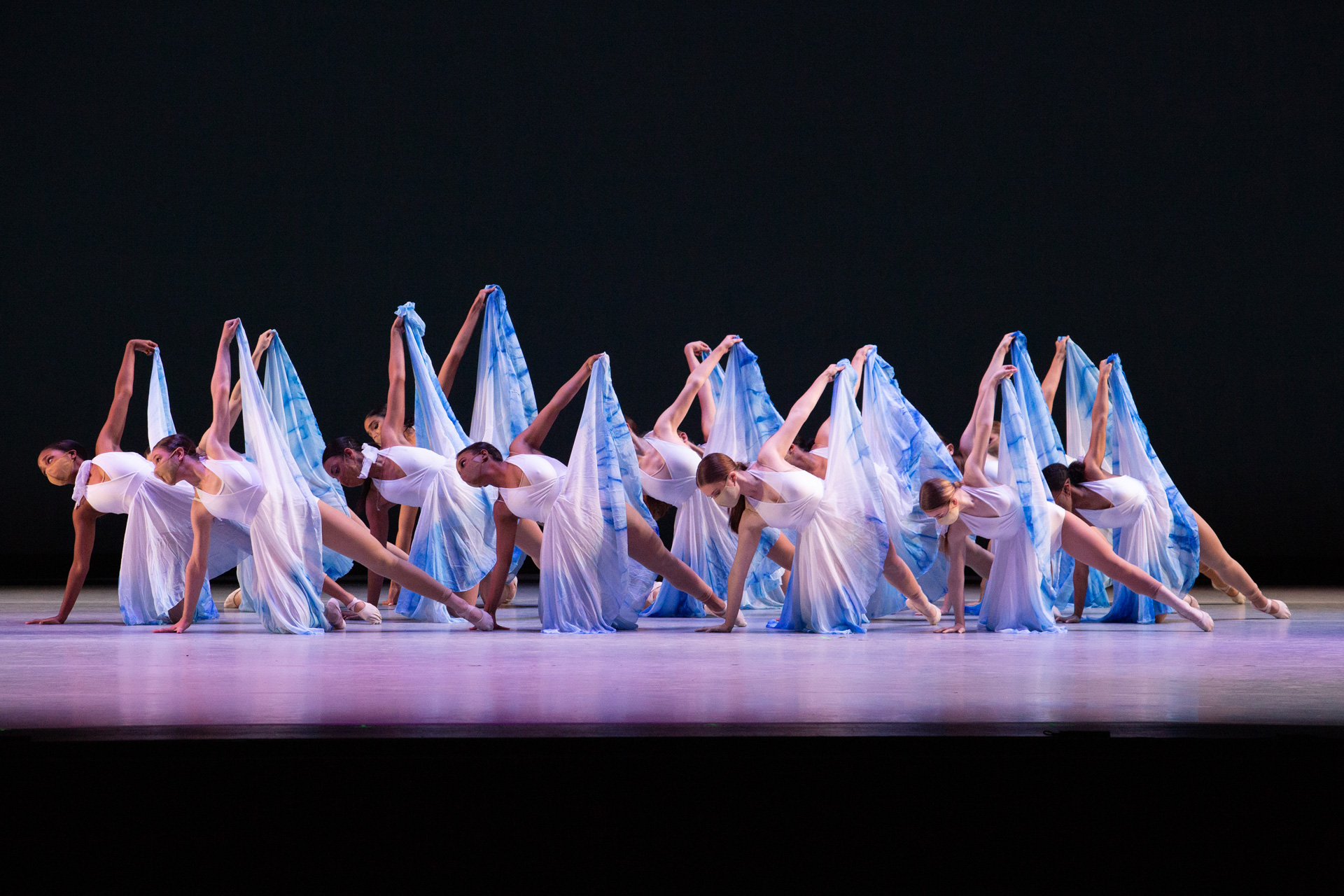 Ballet performers on stage in white dresses dancing.