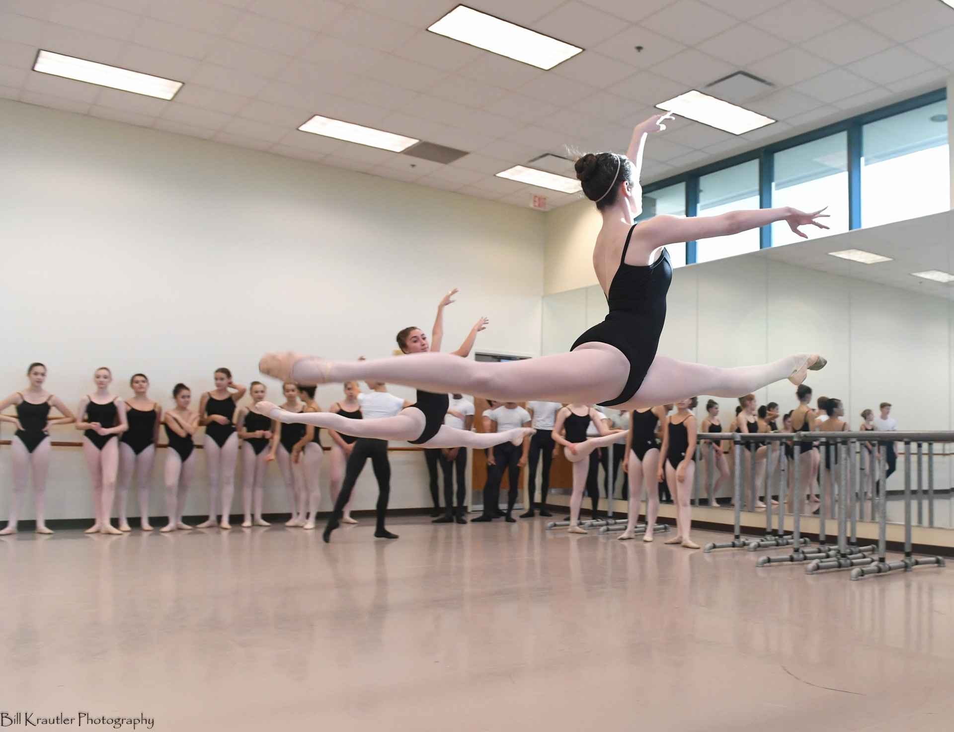Two ballet students in midair pose in ballet studio.